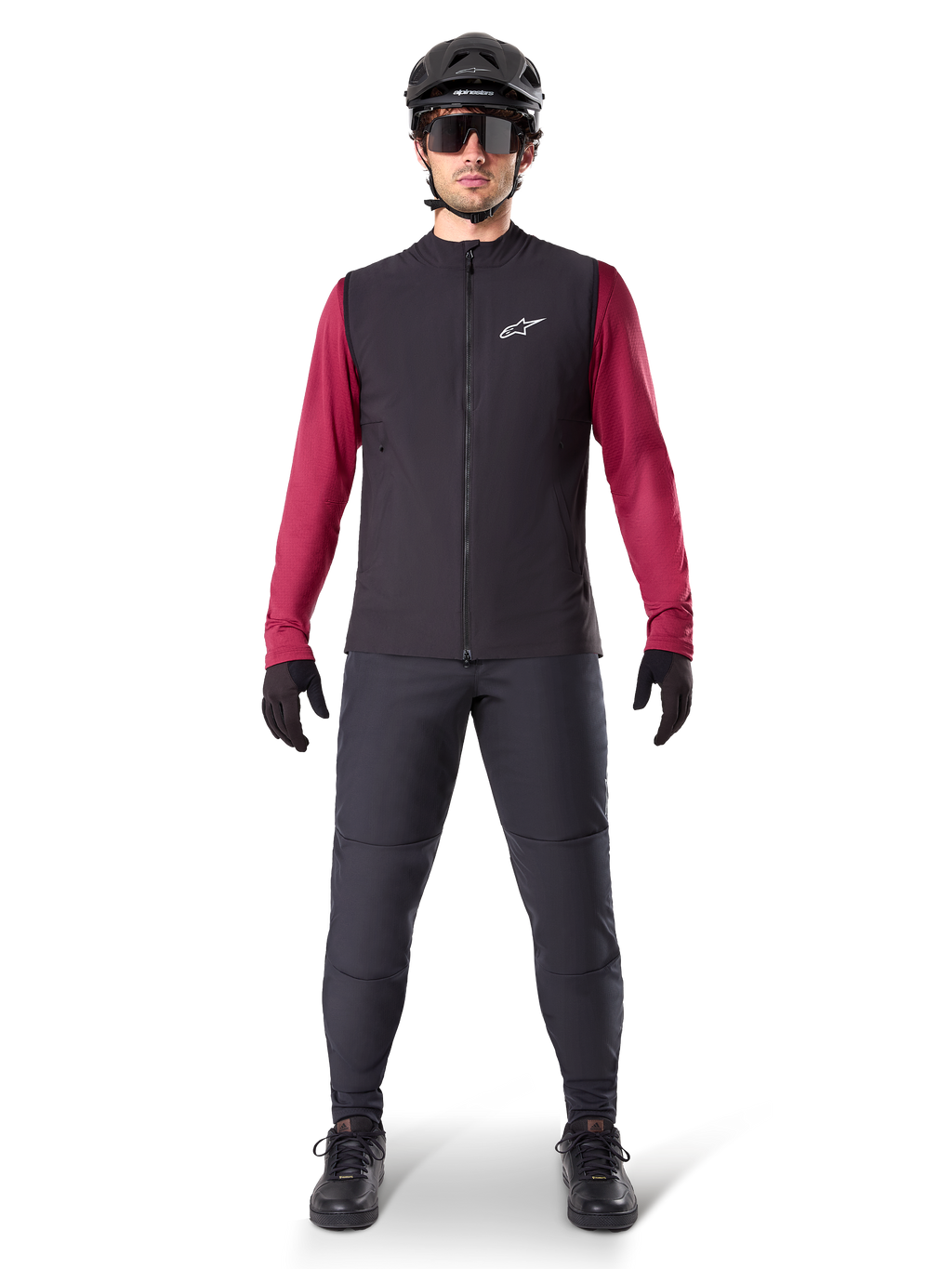 Alpinestars A-Dura Thermoweste, schwarze Radweste getragen über einem weinroten Langarmtrikot, kombiniert mit dunkelgrauer MTB-Hose, schwarzem Helm und Sonnenbrille, technische Mountainbike-Bekleidung für Fahrten bei kaltem Wetter