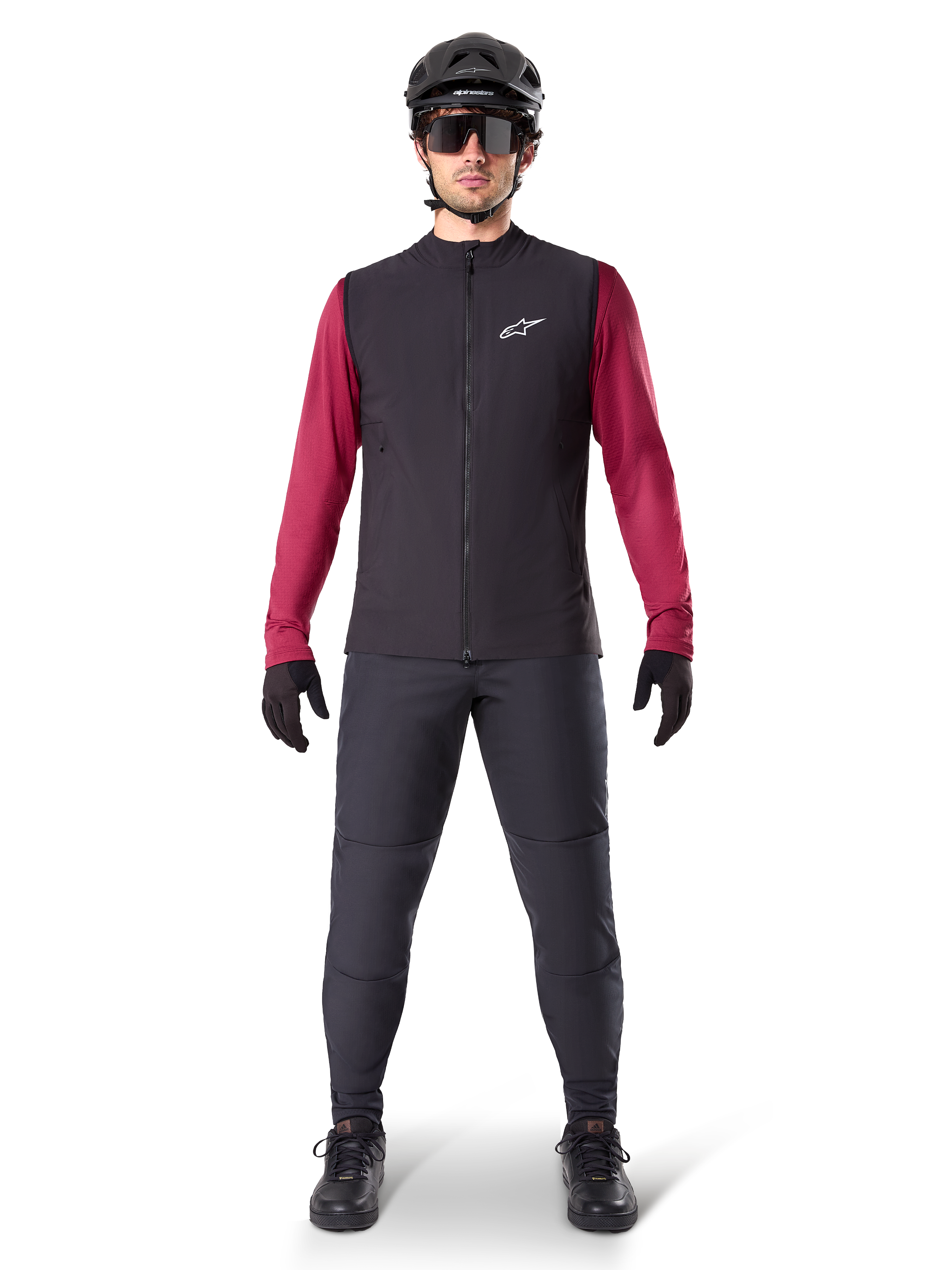 Alpinestars A-Dura Thermoweste, schwarze Radweste getragen über einem weinroten Langarmtrikot, kombiniert mit dunkelgrauer MTB-Hose, schwarzem Helm und Sonnenbrille, technische Mountainbike-Bekleidung für Fahrten bei kaltem Wetter