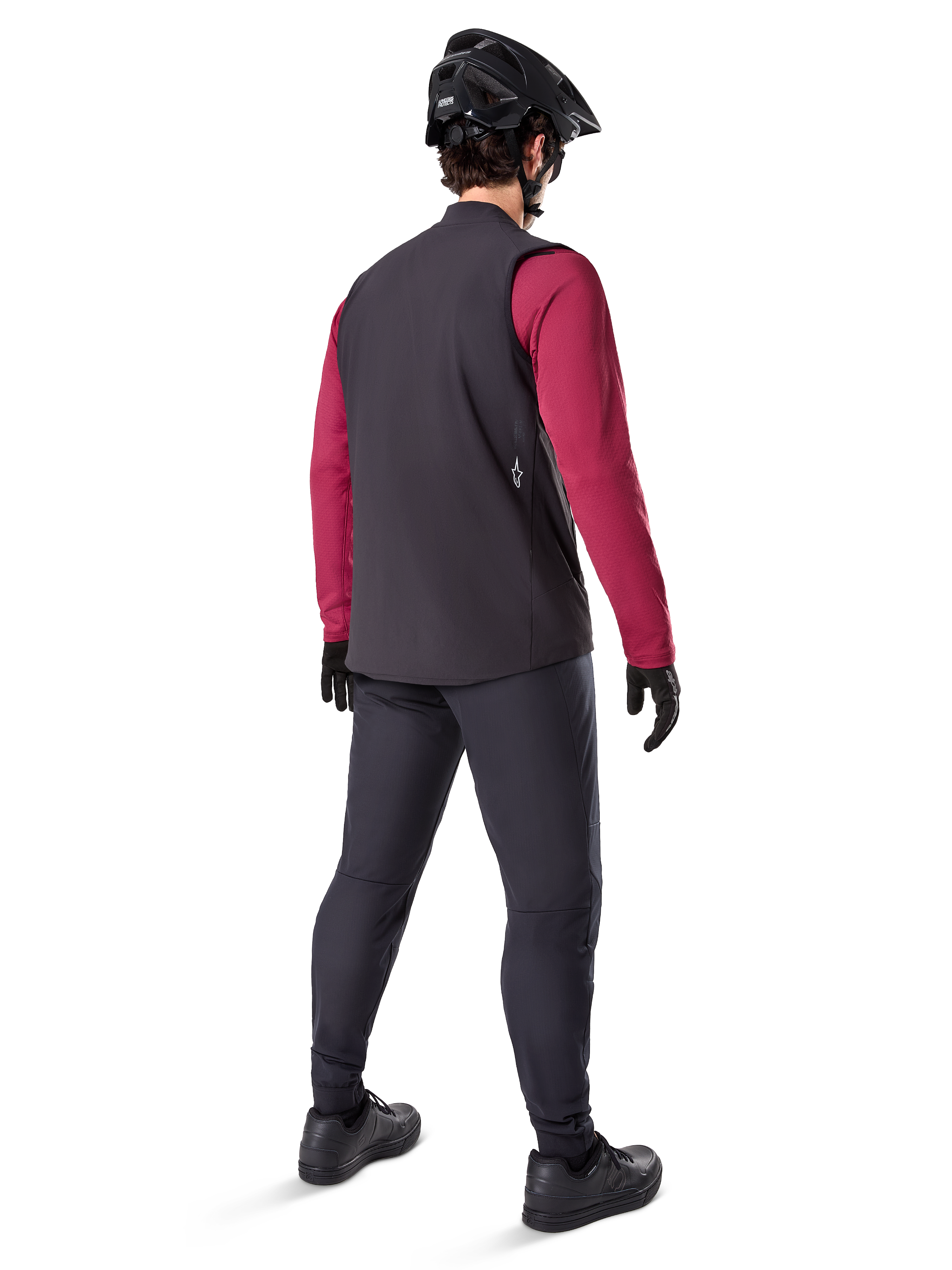 Alpinestars A-Dura Thermoweste, schwarze Fahrradweste, Rückansicht an einem Model mit weinrotem Langarm-Trikot und schwarzer Fahrradhose, kombiniert mit schwarzem Mountainbike-Helm und Handschuhen, technische Ausrüstung für Fahrten bei kaltem Wetter.