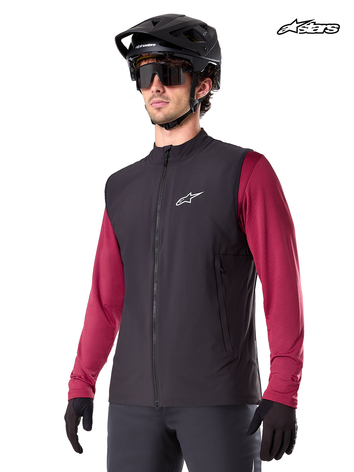 Alpinestars A-Dura Thermoweste, schwarze Mountainbike-Thermoweste für Herren, getragen von einem Model mit Helm und rotem Langarm-Trikot, isoliert für MTB-Fahrten bei kaltem Wetter