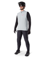 Alpinestars A-Dura Thermal Vest, Titanium gray cycling gilet with a pink logo, worn by a model with a black long-sleeve shirt, dark gray pants, and a black mountain bike helmet, performance gear for cold-weather riding