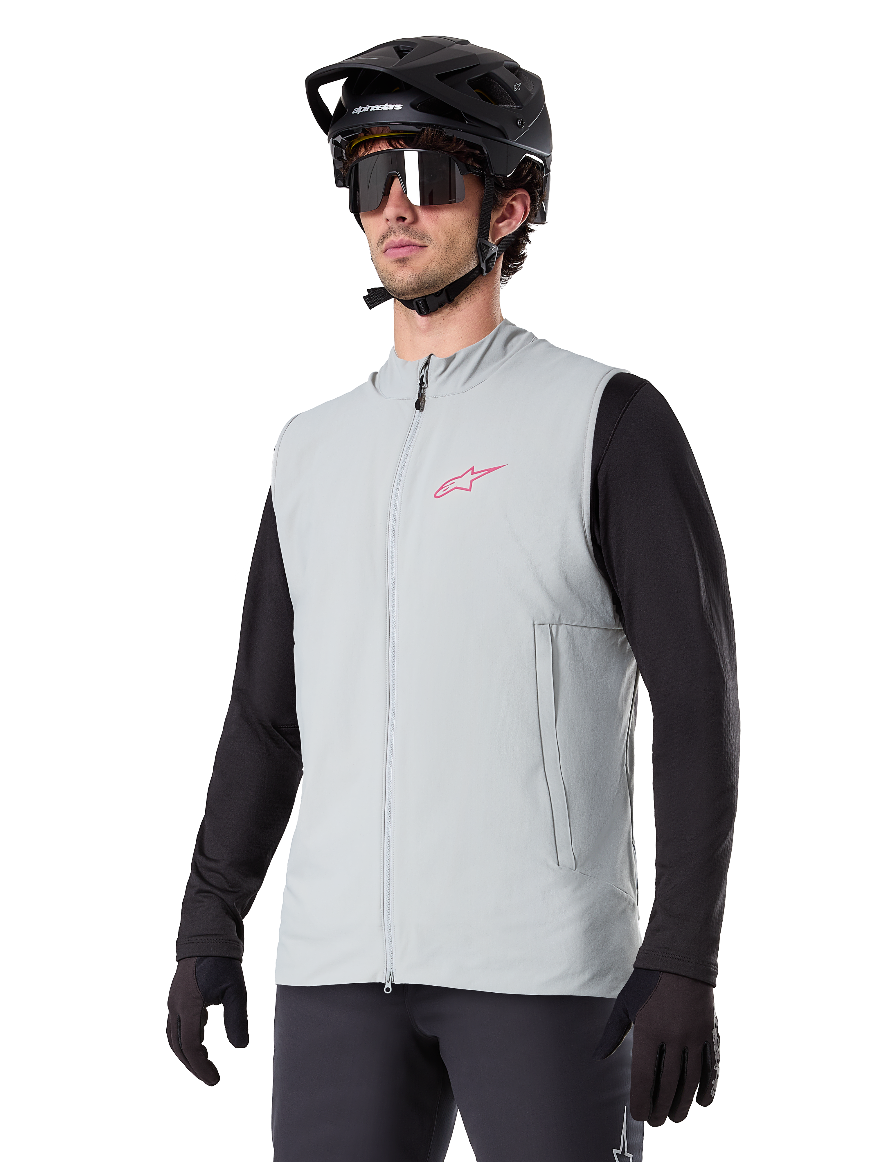 Alpinestars A-Dura Thermoweste, Titanium-Grau, isolierte Fahrradweste, getragen über einem schwarzen Langarmshirt mit schwarzem Mountainbike-Helm und Handschuhen, mit pinkfarbenem Logo auf der Brust und vertikalen Reißverschlusstaschen
