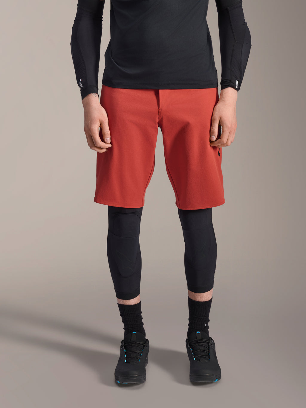 Alpinestars A-Motion Plasma Knee Sleeve, Black MTB knee protector, worn with red shorts and black long-sleeve top, slim-profile ergonomic design, lightweight mesh construction for off-road riding