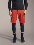 Alpinestars A-Motion Plasma Knee Sleeve, Black MTB knee protector, worn with red shorts and black long-sleeve top, slim-profile ergonomic design, lightweight mesh construction for off-road riding