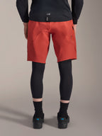 Alpinestars A-Motion Plasma Knee Sleeve, black MTB knee protectors, back view worn under red mountain bike shorts with a black jersey and technical cycling shoes, protective gear for mountain biking