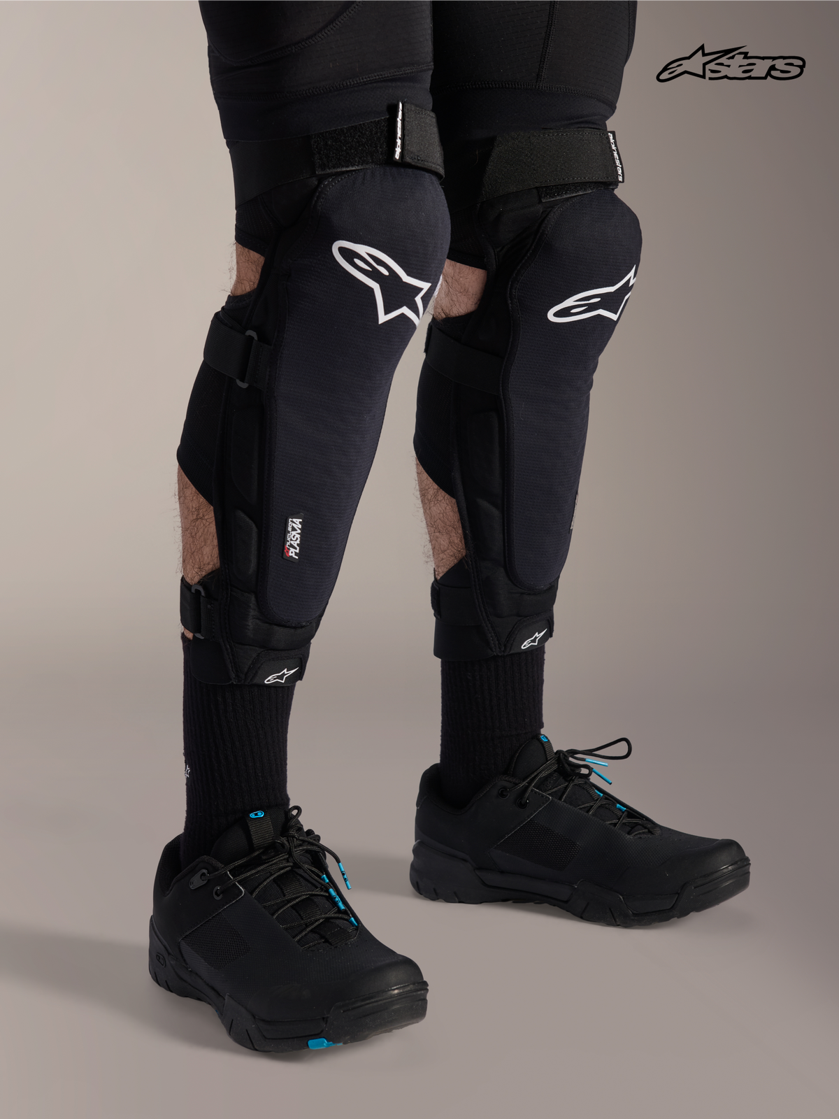 Alpinestars A-Impact Plasma Pro Knie-/Schienbeinschutz, Mountainbike-Knieschützer in Schwarz mit weißem Logo, getragen von einem Model mit dreifach Riemenverschluss und Nucleon Plasma-Technologie