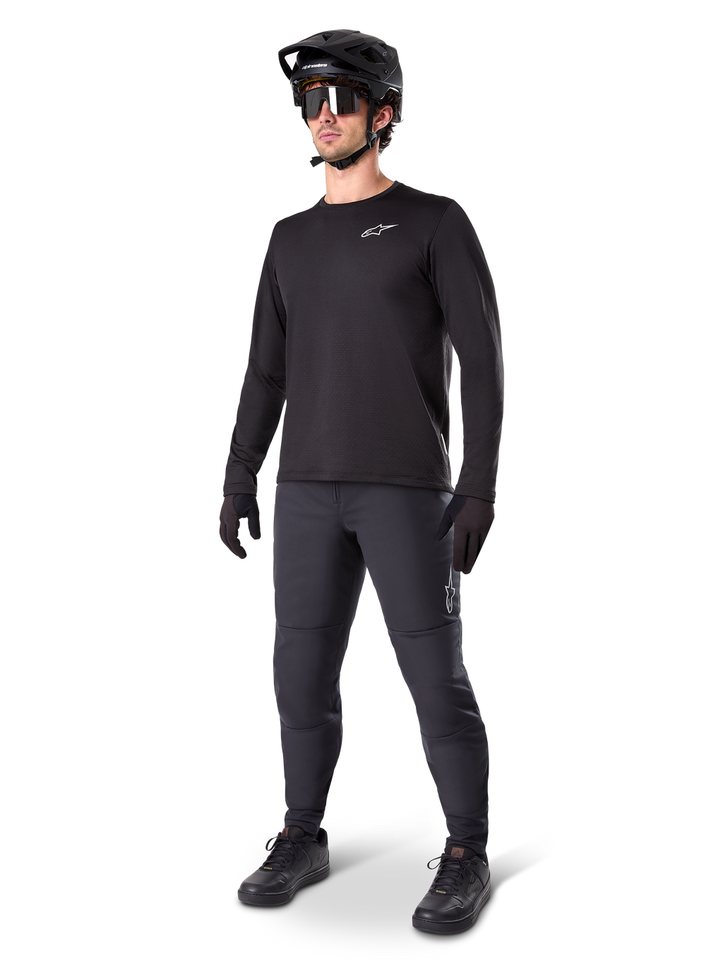 Mountainbike-Fahrer trägt Alpinestars A-Dura Thermo-Hose, Schwarz, kombiniert mit schwarzem Langarm-Trikot, schwarzem Helm und Sonnenbrille, mit silbernem Alpinestars-Logo auf dem linken Oberschenkel, konzipiert für Trail-Fahrten bei kaltem Wetter
