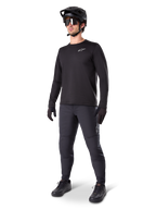 Mountainbike-Fahrer trägt Alpinestars A-Dura Thermo-Hose, Schwarz, kombiniert mit schwarzem Langarm-Trikot, schwarzem Helm und Sonnenbrille, mit silbernem Alpinestars-Logo auf dem linken Oberschenkel, konzipiert für Trail-Fahrten bei kaltem Wetter