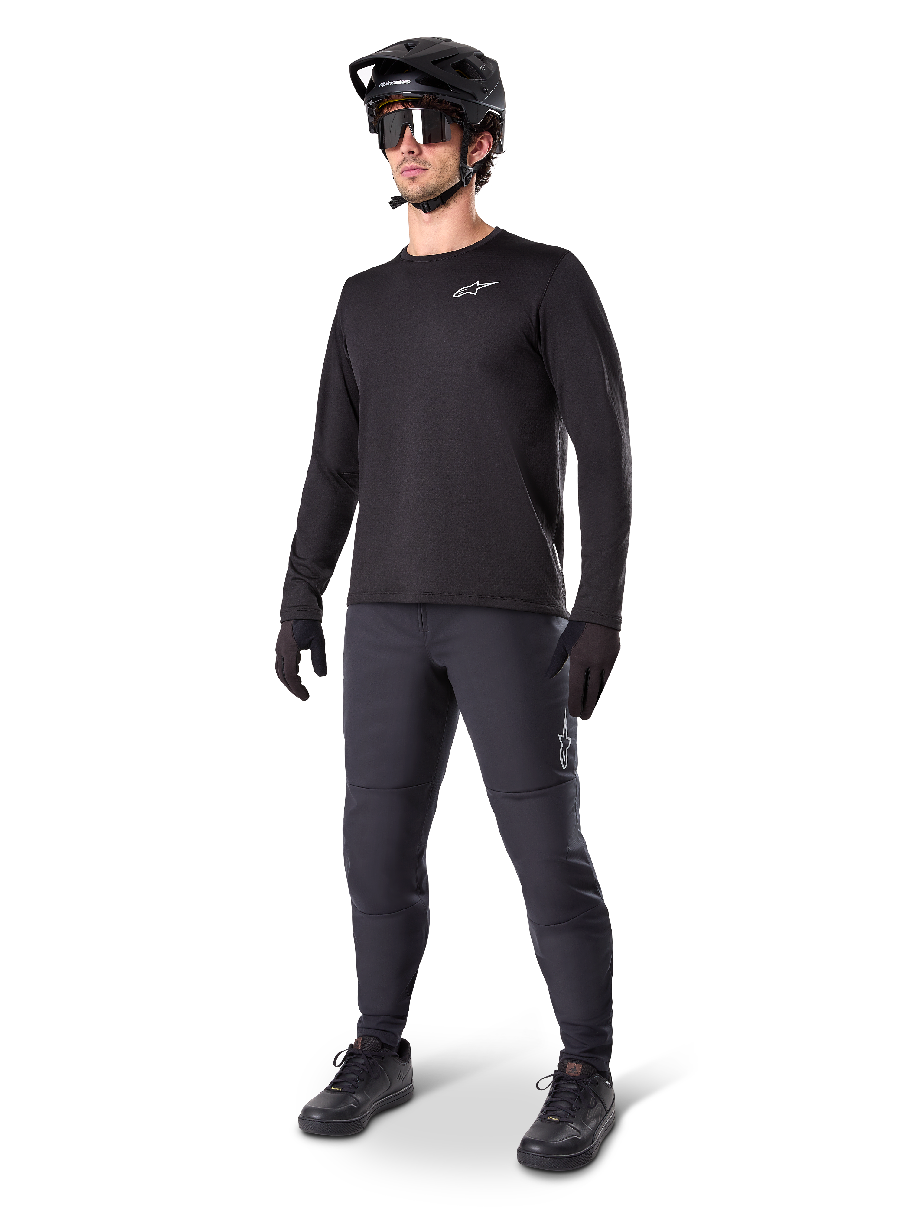 Mountainbike-Fahrer trägt Alpinestars A-Dura Thermo-Hose, Schwarz, kombiniert mit schwarzem Langarm-Trikot, schwarzem Helm und Sonnenbrille, mit silbernem Alpinestars-Logo auf dem linken Oberschenkel, konzipiert für Trail-Fahrten bei kaltem Wetter