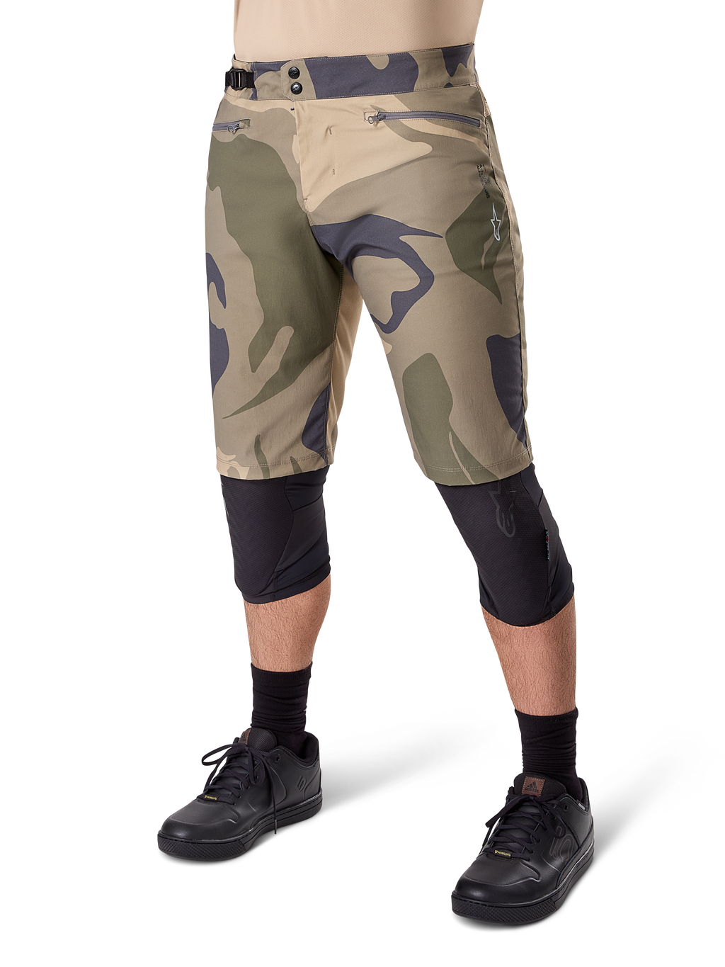 Alpinestars A-Dura Camo Liner Shorts, Mountainbike-Shorts, braunes Camo-Muster, Vorderansicht mit Reißverschlusstaschen und seitlichen Taillenverstellern, getragen mit schwarzen Knieschonern und schwarzen Fahrradschuhen, strapazierfähige MTB-Ausrüstung
