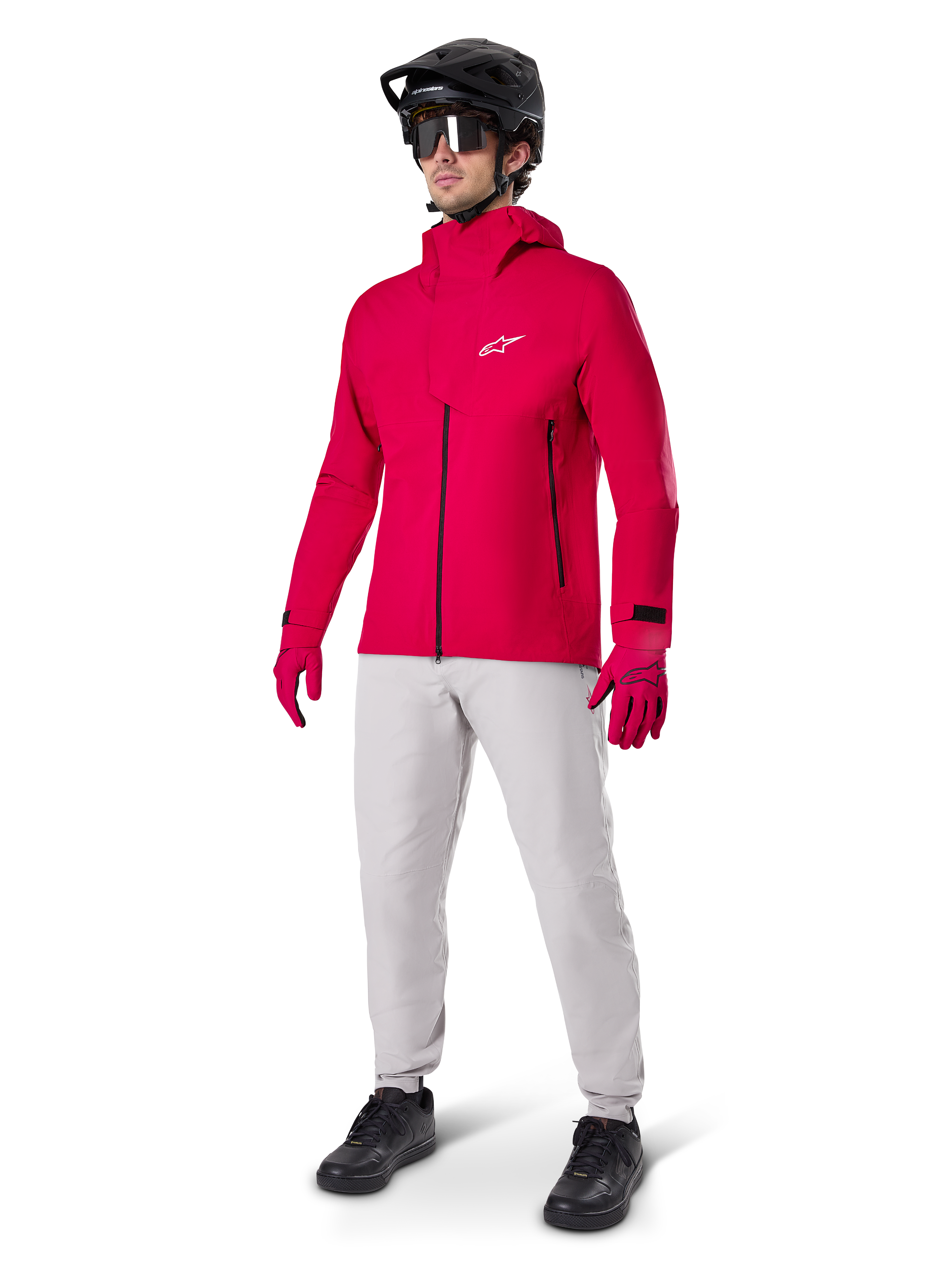 Model wearing Alpinestars A-Dura Waterproof Pants in Titanium gray, paired with a bright red waterproof jacket and matching gloves, black mountain bike helmet with goggles, and black shoes, full mountain biking gear for wet trail conditions