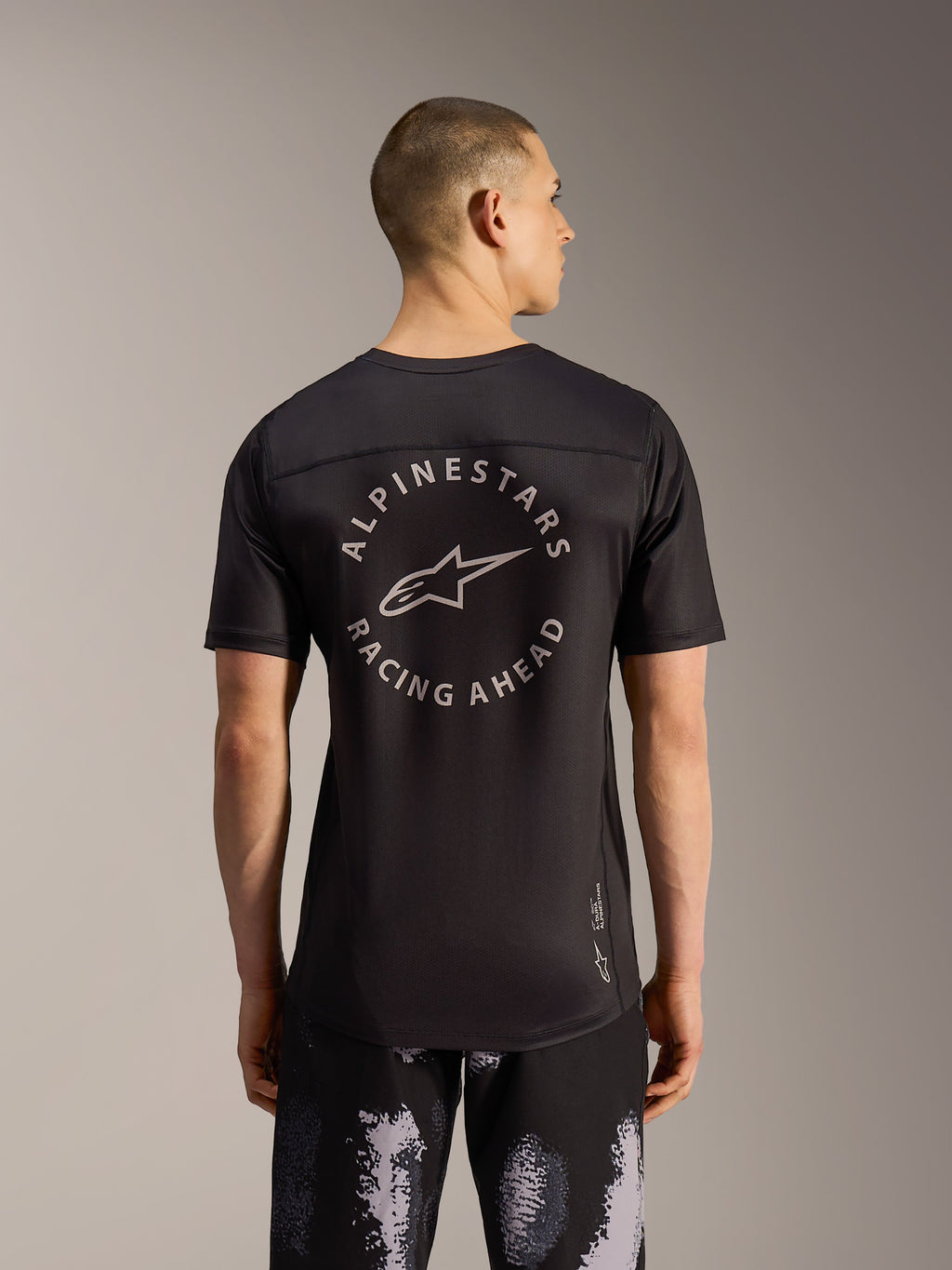 Alpinestars A-Dura Ride Shorts in Black Camo und schwarzes MTB-Trikot mit rundem Rückenlogo, Rückansicht am Model.
