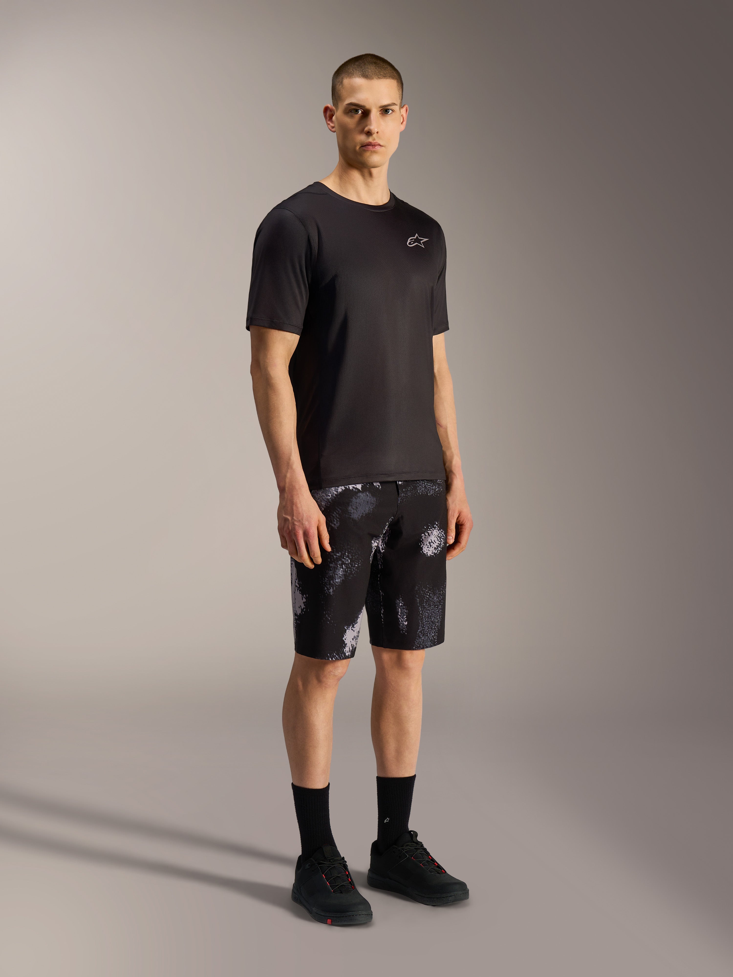 A-Dura Ride MTB-Shorts in Black Camo mit grauem Camouflage-Muster, kombiniert mit schwarzem Jersey und Schuhen.