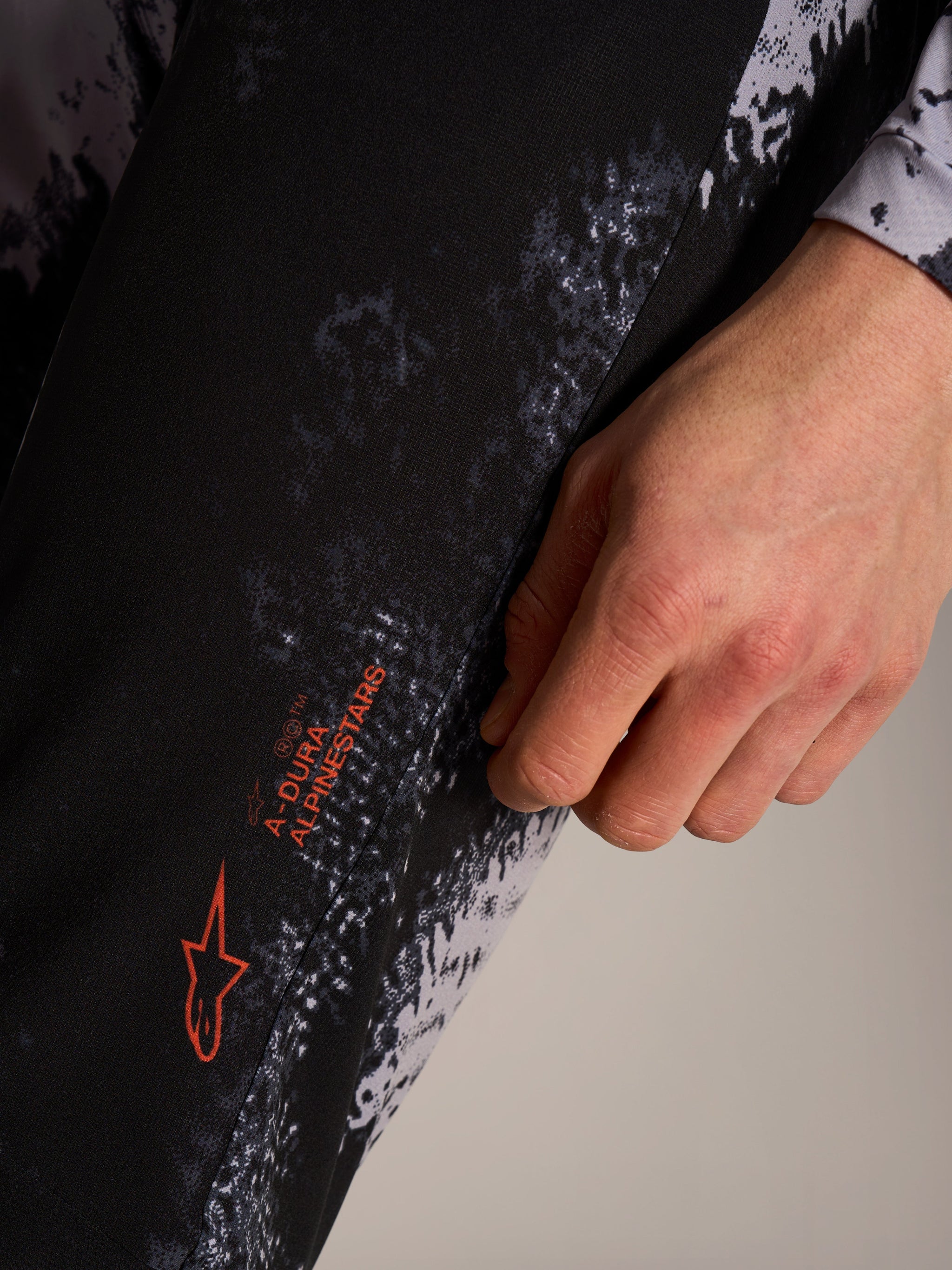 Alpinestars A-Dura Ride Hose in Black Camo mit orangen Logo-Details auf technischem MTB-Stretchgewebe.