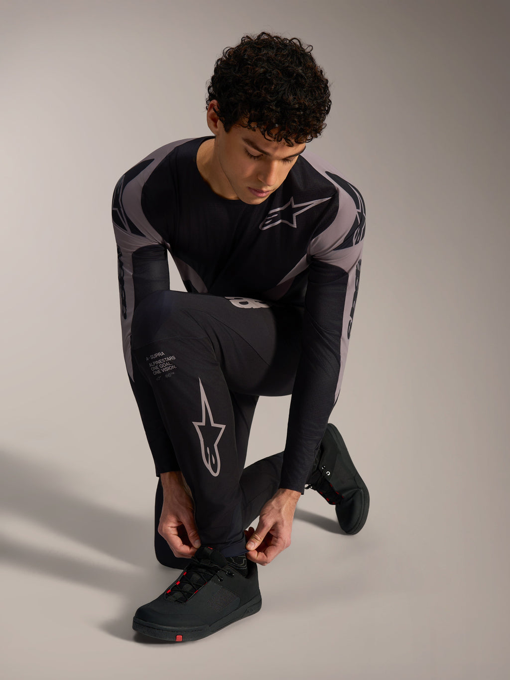 Schwarze Alpinestars A-Supra Elite MTB-Hose mit grauen Logos, getragen von einem knienden Modell.