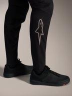 Schwarze A-Supra Elite MTB-Hose mit silbernem Astars-Logo am Unterschenkel, für High-Performance-Mountainbiking.