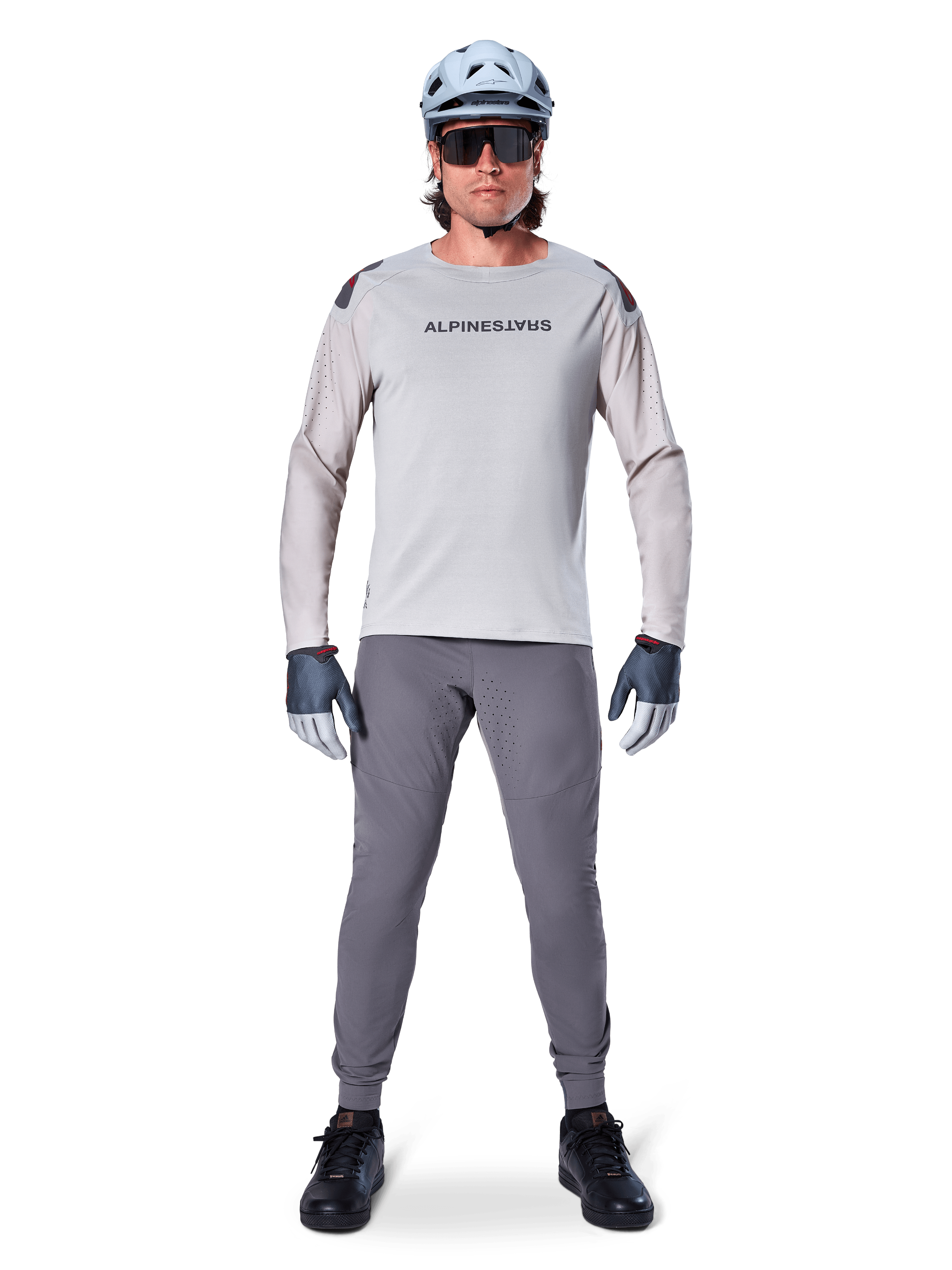 Alpinestars A-Aria Elite Hose, dunkelgraue Mountainbike-Hose, getragen von einem Fahrer in hellgrauem Langarmtrikot, hellblauem Helm und schwarzen Schuhen, mit sichtbaren Laserperforationen an den Beininnenseiten und schmaler Performance-Passform.