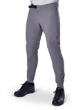Alpinestars A-Aria Elite Hose, dunkelgraue MTB-Hose, laserperforierte Einsätze an den Oberschenkeln, schwarzer Magnetverschluss, Reißverschlusstasche, rotes Logo-Detail, schmale Performance-Passform, getragen mit schwarzen Schuhen