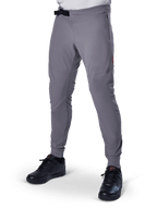 Alpinestars A-Aria Elite Hose, dunkelgraue MTB-Hose, laserperforierte Einsätze an den Oberschenkeln, schwarzer Magnetverschluss, Reißverschlusstasche, rotes Logo-Detail, schmale Performance-Passform, getragen mit schwarzen Schuhen