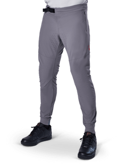 Alpinestars A-Aria Elite Pants, Dark Gray MTB Pants, laser perforated panels on thighs, black magnetic buckle closure, zippered pocket, red logo detail, slim performance fit, worn with black shoes