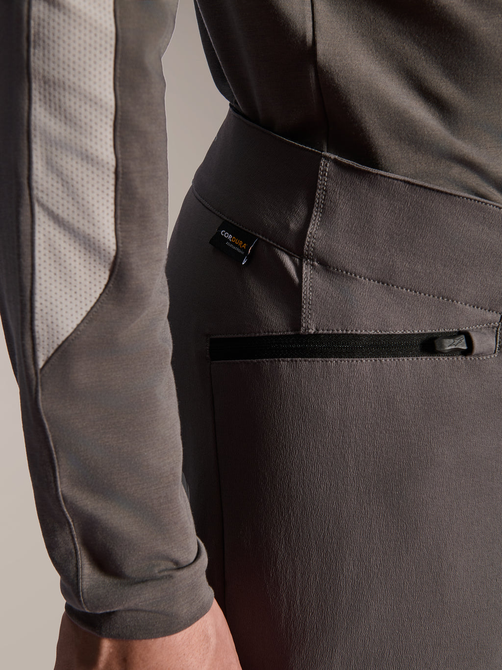 Alpinestars A-Dura Elite Pants, dunkelgraue Mountainbike-Hose, Detailansicht der seitlichen Reißverschlusstasche und des Cordura-Stoffetiketts, strapazierfähiges 4-Wege-Stretch-Textil für Offroad-Performance