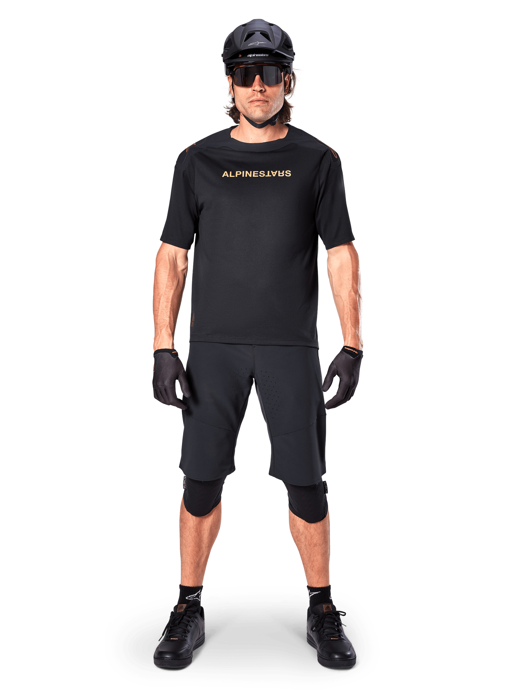 Male mountain bike rider wearing Alpinestars A-Aria Elite Shorts in Black, paired with a matching black Alpinestars short-sleeve jersey, black helmet, gloves, and knee guards, complete off-road cycling gear outfit