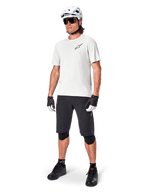 Male mountain biker wearing Alpinestars A-Aria Shorts, Black cycling shorts, styled with a white short-sleeve jersey, white mountain bike helmet, and black performance gear, full outfit for off-road trail riding