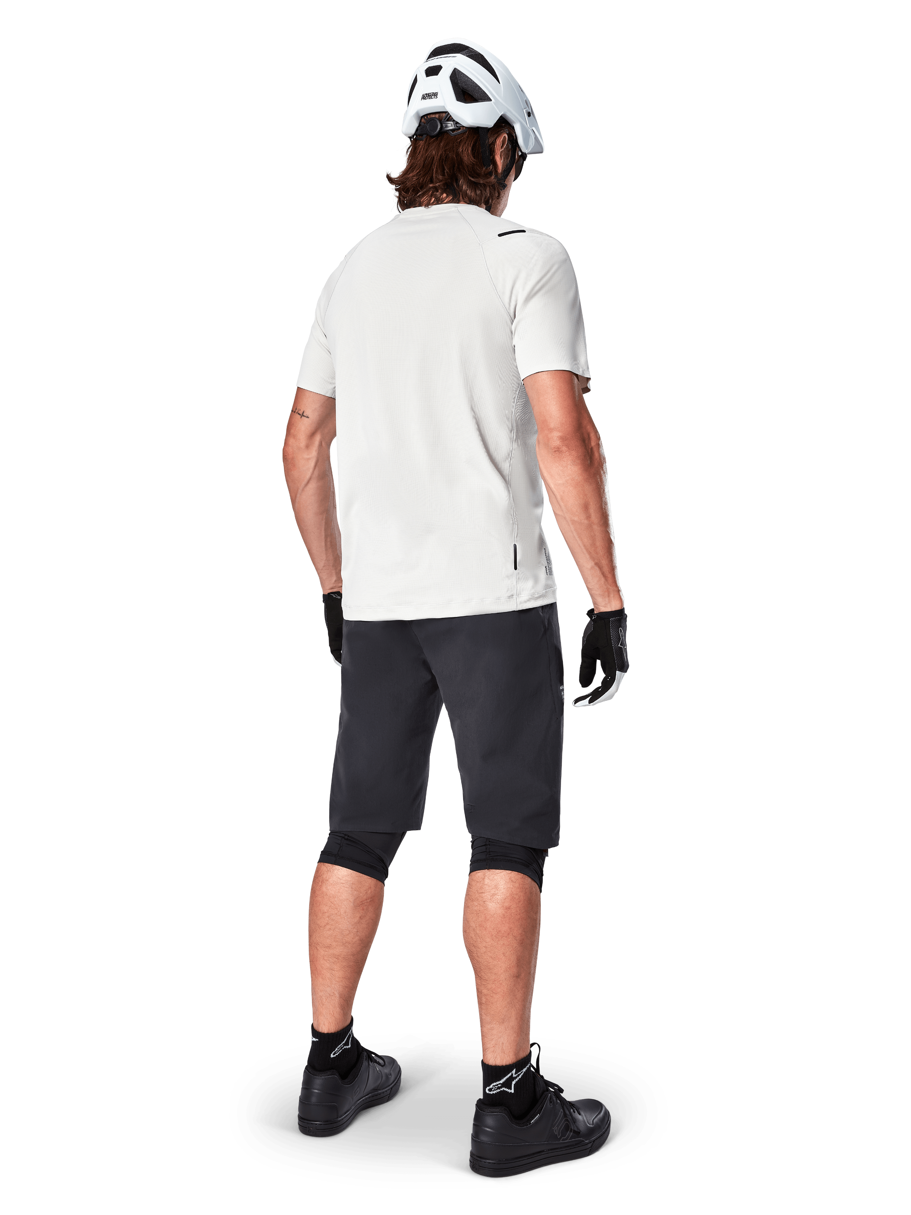 Mountain biker from behind wearing Alpinestars A-Aria Shorts in Black, white performance short-sleeve jersey, white helmet, black gloves, and black mountain bike shoes, cycling gear for trail riding