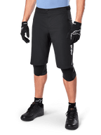 Alpinestars A-Dura Elite Shorts, Black MTB Mountain Biking Shorts, worn with light blue shirt and black knee protection, featuring a secure snap closure and zippered pocket, paired with black cycling shoes and gloves for a complete off-road outfit.