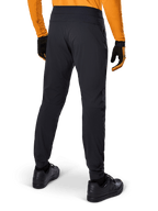 Alpinestars A-Dura Hose, schwarze MTB-Hose, Rückansicht, getragen mit einem orangefarbenen Langarm-Trikot und schwarzen Handschuhen, mit elastischen Bündchen und strapazierfähigem Textilmaterial für Mountainbiking.