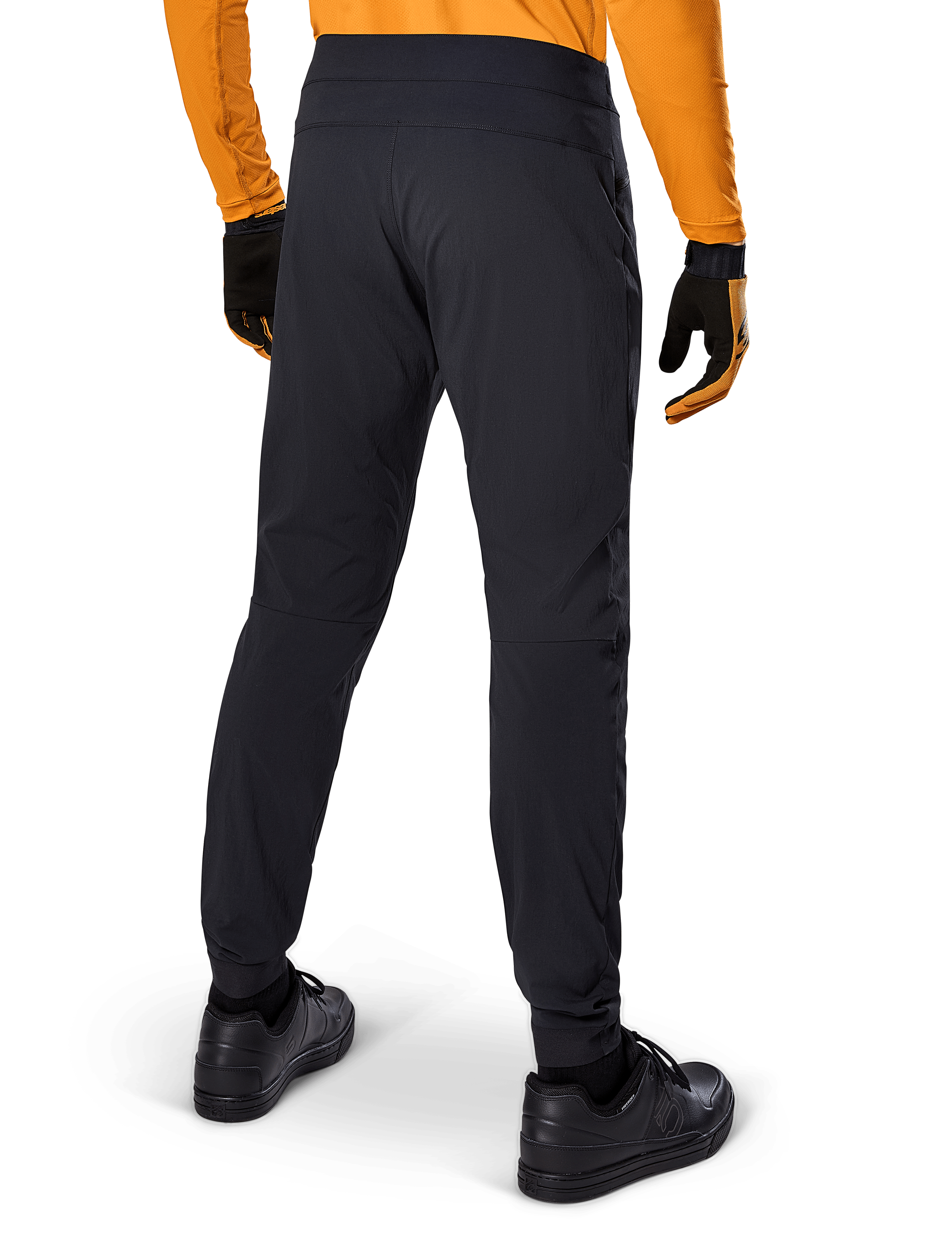 Alpinestars A-Dura Hose, schwarze MTB-Hose, Rückansicht, getragen mit einem orangefarbenen Langarm-Trikot und schwarzen Handschuhen, mit elastischen Bündchen und strapazierfähigem Textilmaterial für Mountainbiking.