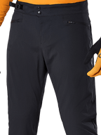 Alpinestars A-Dura Hose, schwarze MTB-Radhose, Detailansicht mit doppeltem Druckknopfverschluss, verstellbarem seitlichem Taillenversteller und Reißverschlusstaschen, kombiniert mit einem orangefarbenen Trikot und Handschuhen