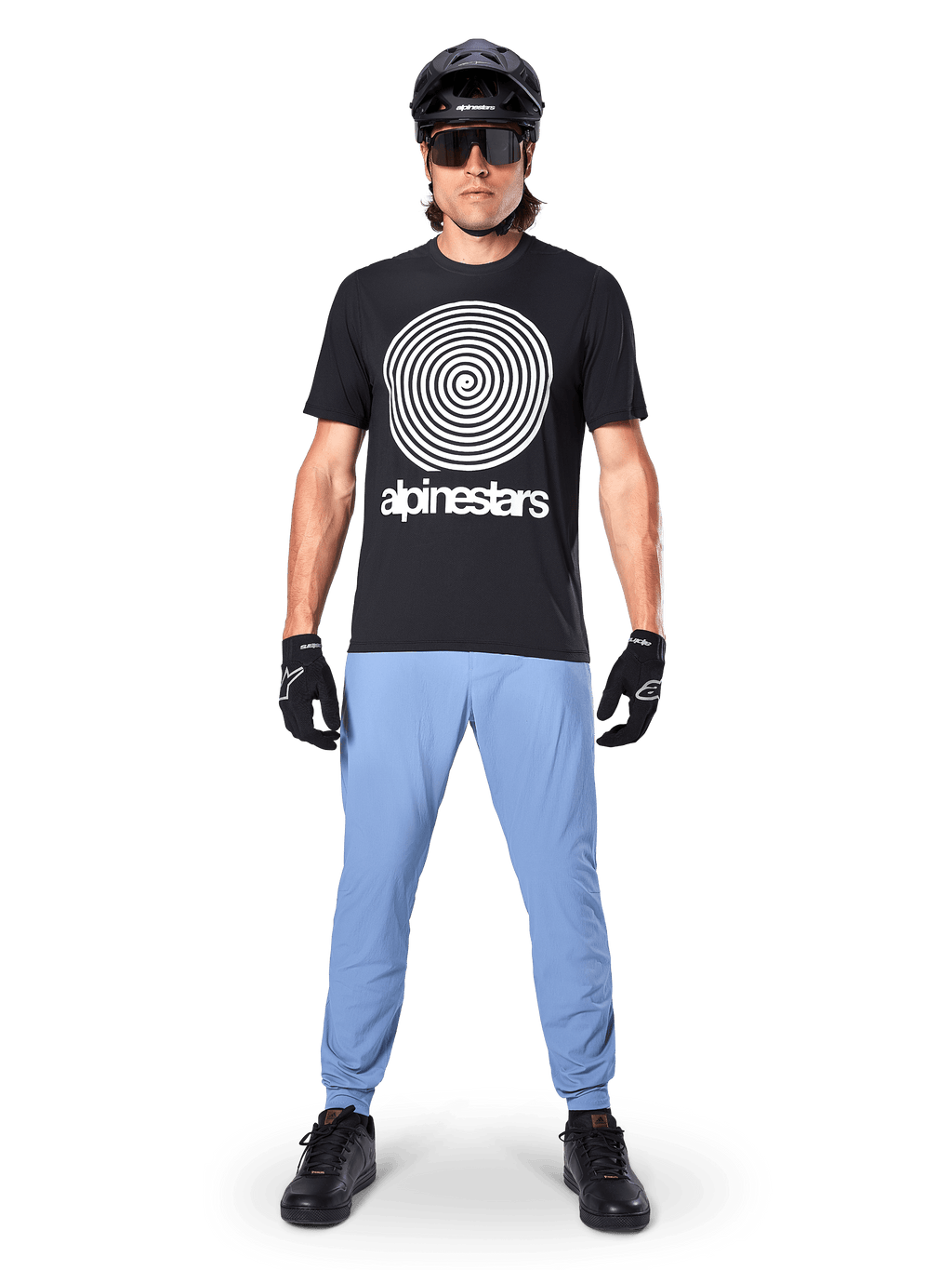 Alpinestars A-Dura Hose, Infinity Blue, MTB-Hose getragen mit einem schwarzen T-Shirt mit Spiralgrafik, schwarzen Handschuhen und einem schwarzen Helm, aus strapazierfähigem Stretch-Gewebe und mit elastischen Bündchen, Performance-Mountainbike-Ausrüstung