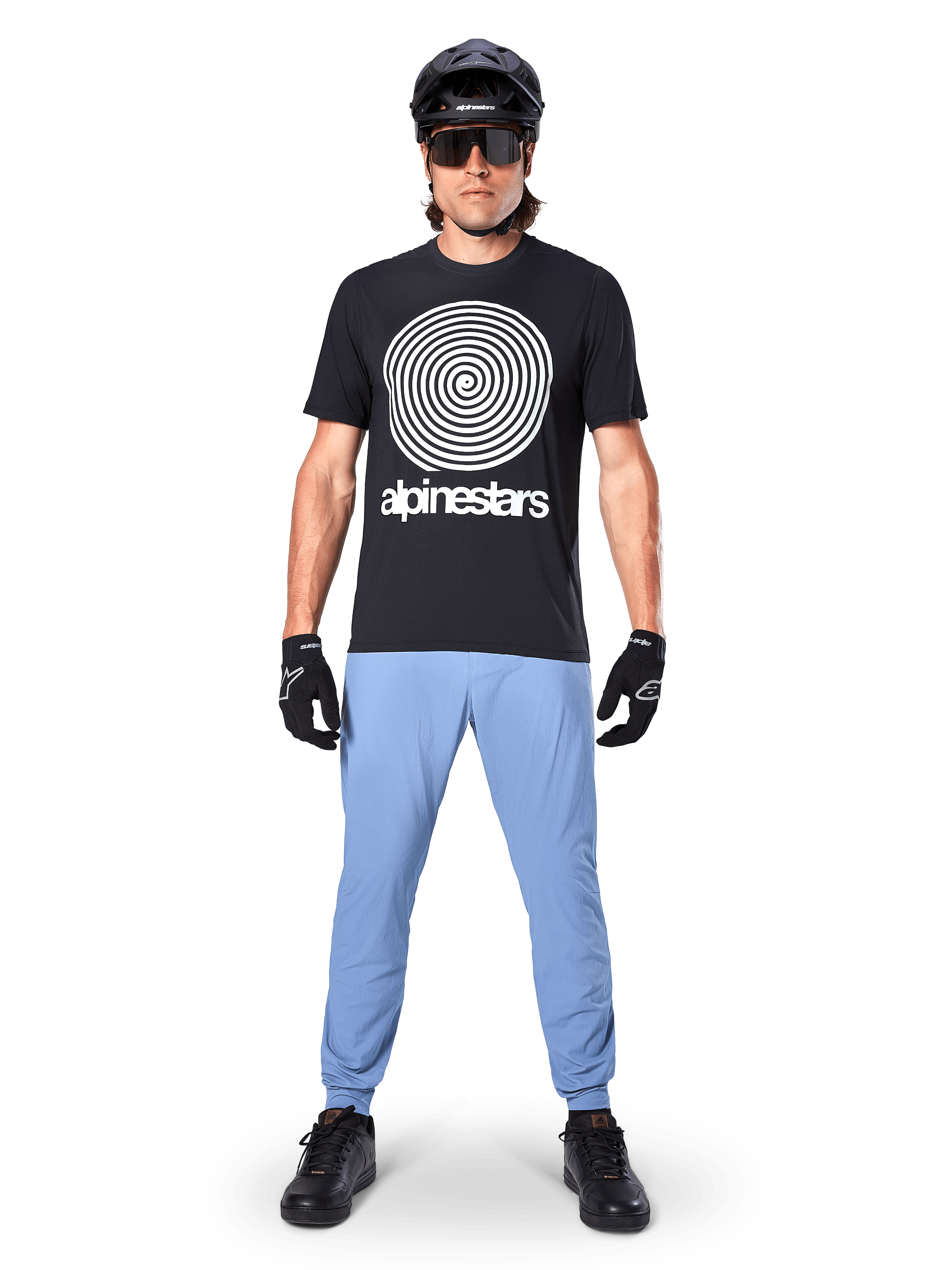 Alpinestars A-Dura Hose, Infinity Blue, MTB-Hose getragen mit einem schwarzen T-Shirt mit Spiralgrafik, schwarzen Handschuhen und einem schwarzen Helm, aus strapazierfähigem Stretch-Gewebe und mit elastischen Bündchen, Performance-Mountainbike-Ausrüstung