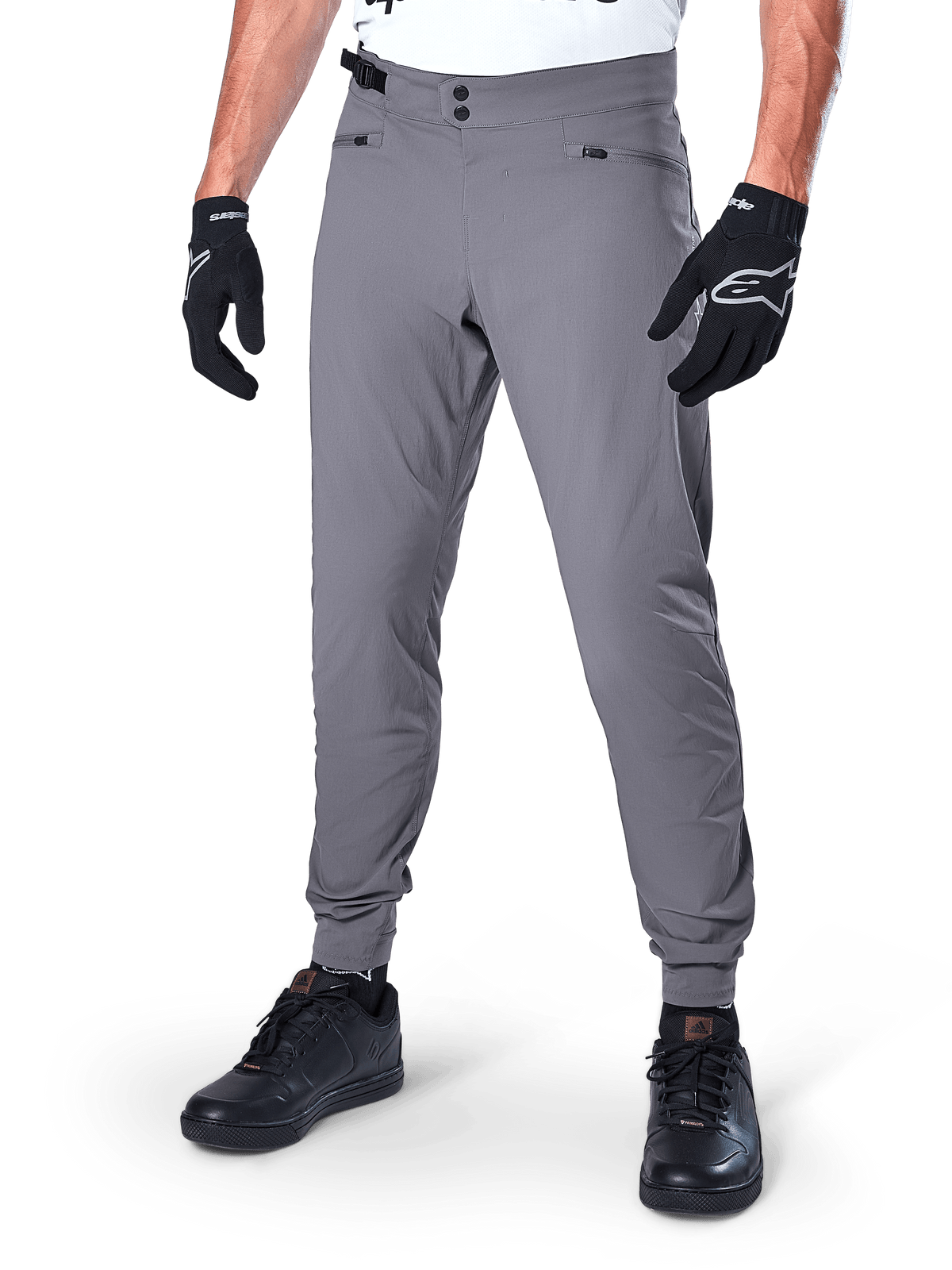 Alpinestars A-Dura Hose, dunkelgraue MTB-Hose, mit doppeltem Druckknopfverschluss und Reißverschlusstaschen, elastische Bündchen, getragen mit schwarzen Fahrradhandschuhen und schwarzen Sneakern