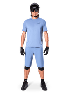Model trägt Alpinestars A-Dura Shorts in Infinity Blue, passendes hellblaues Trikot, schwarzen Mountainbike-Helm, schwarze Sonnenbrille, schwarze Handschuhe und Knieschoner, komplettes MTB-Outfit für Trailfahrten