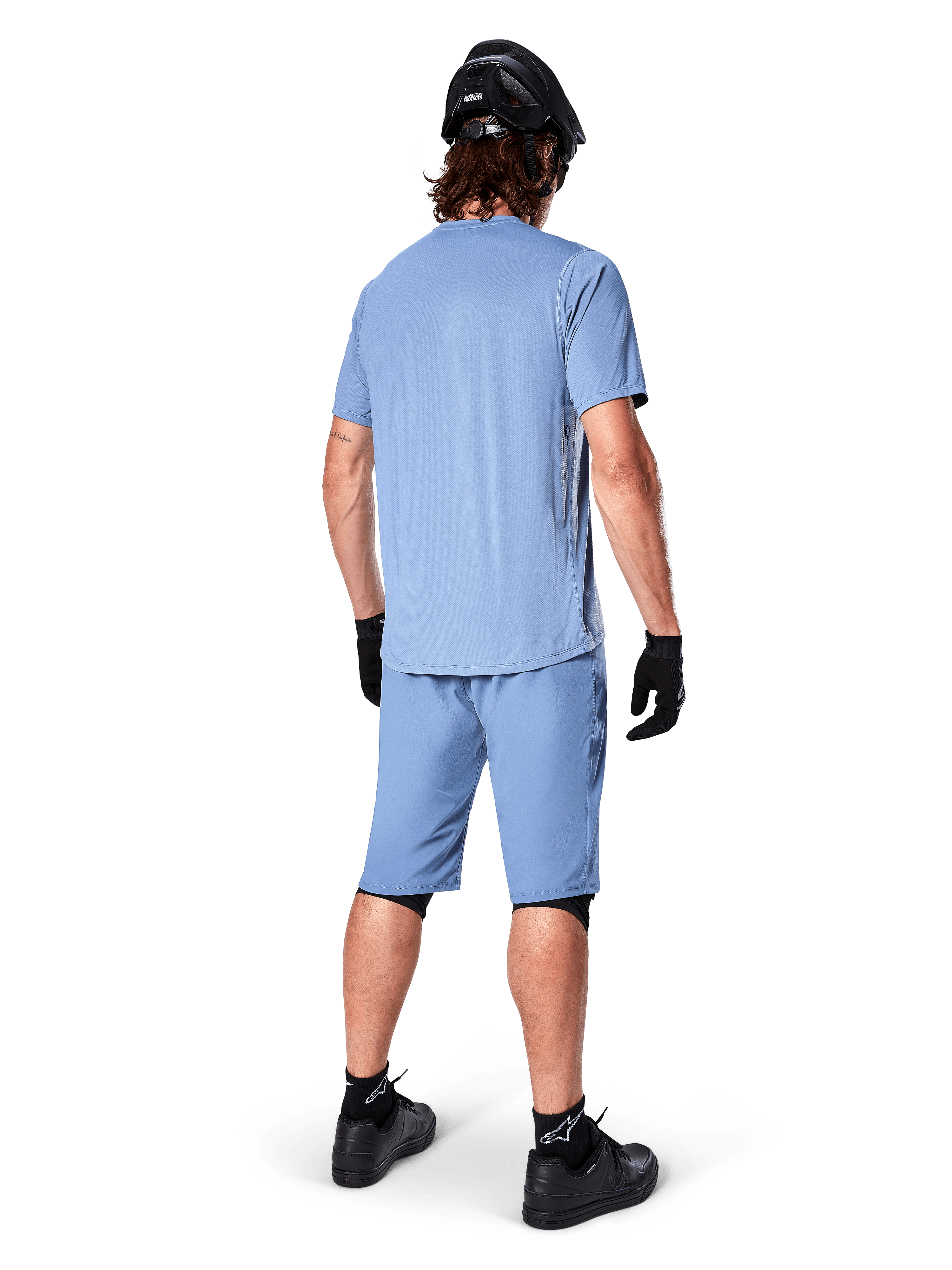 Rückansicht eines Mountainbikers in Alpinestars A-Dura Shorts in Infinity Blue, passendes Kurzarmtrikot, schwarzer Helm, schwarze Handschuhe und schwarze Schuhe, abgestimmte Performance-Ausrüstung für MTB-Trailfahrten