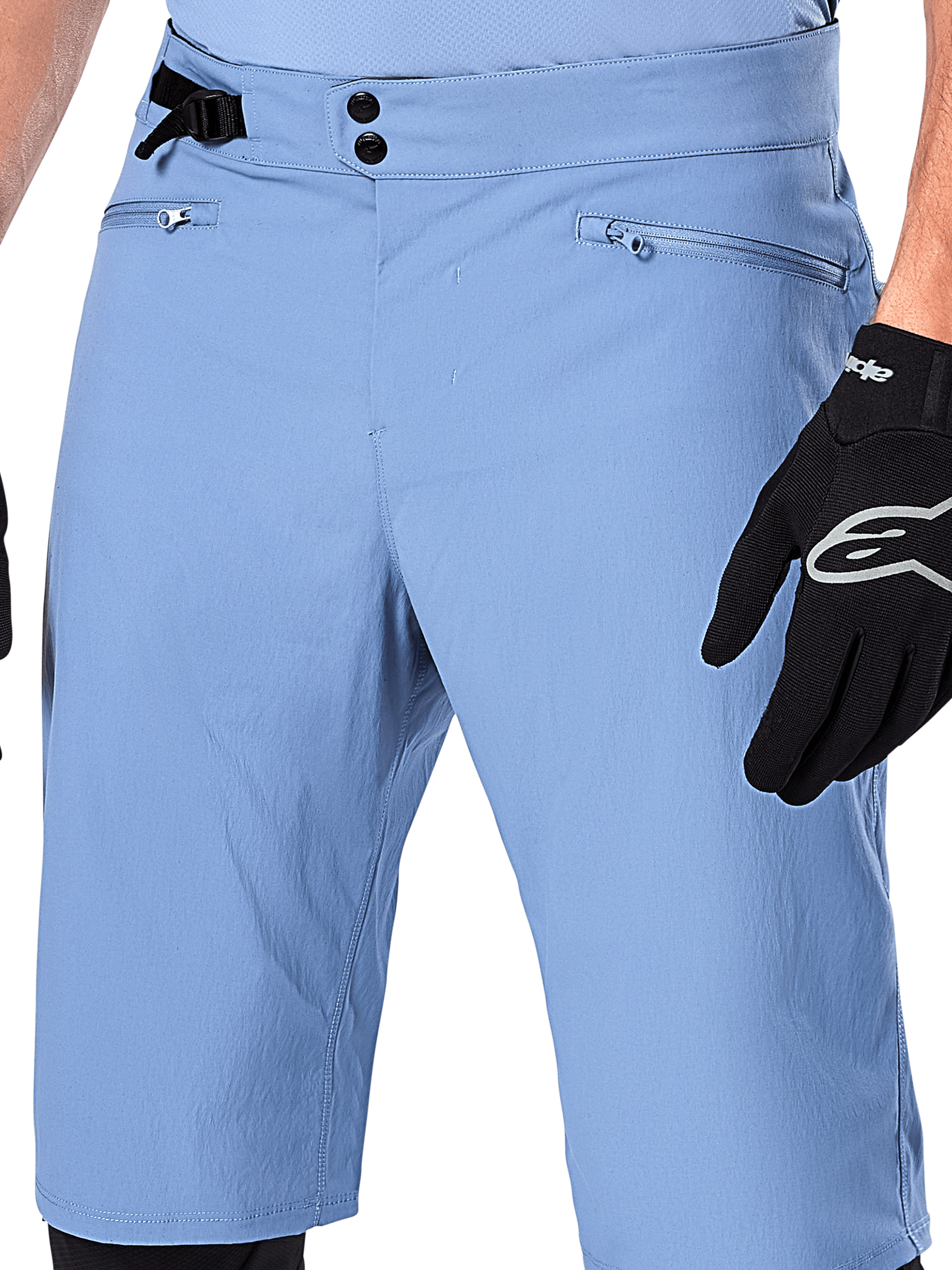 Alpinestars A-Dura Shorts, Mountainbike-Shorts in Infinity Blue, Nahaufnahme der Taille mit doppeltem Druckknopfverschluss, verstellbarem seitlichem Taillenversteller und Reißverschlusstaschen mit Mesh-Futter, getragen mit einem schwarzen Alpinestars-Handschuh
