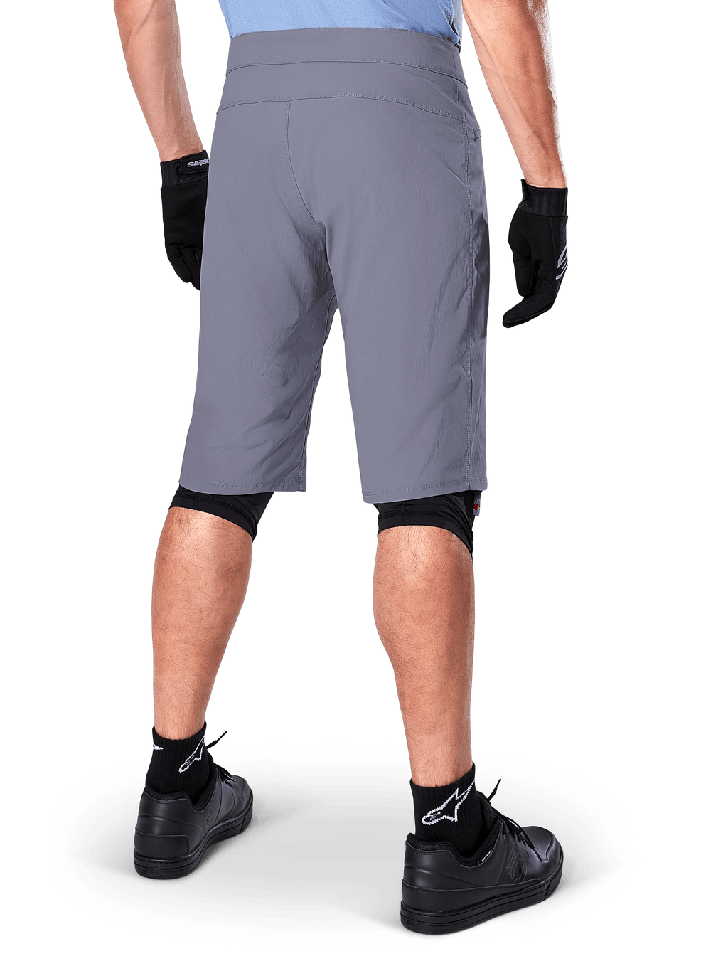 Alpinestars A-Dura Shorts, dunkelgraue Mountainbike-Shorts, Rückansicht an einem Fahrer, getragen mit schwarzen Handschuhen, schwarzen Knie-Linern und schwarzen Socken mit Alpinestars-Logo, strapazierfähige Konstruktion für den Offroad-Radsport