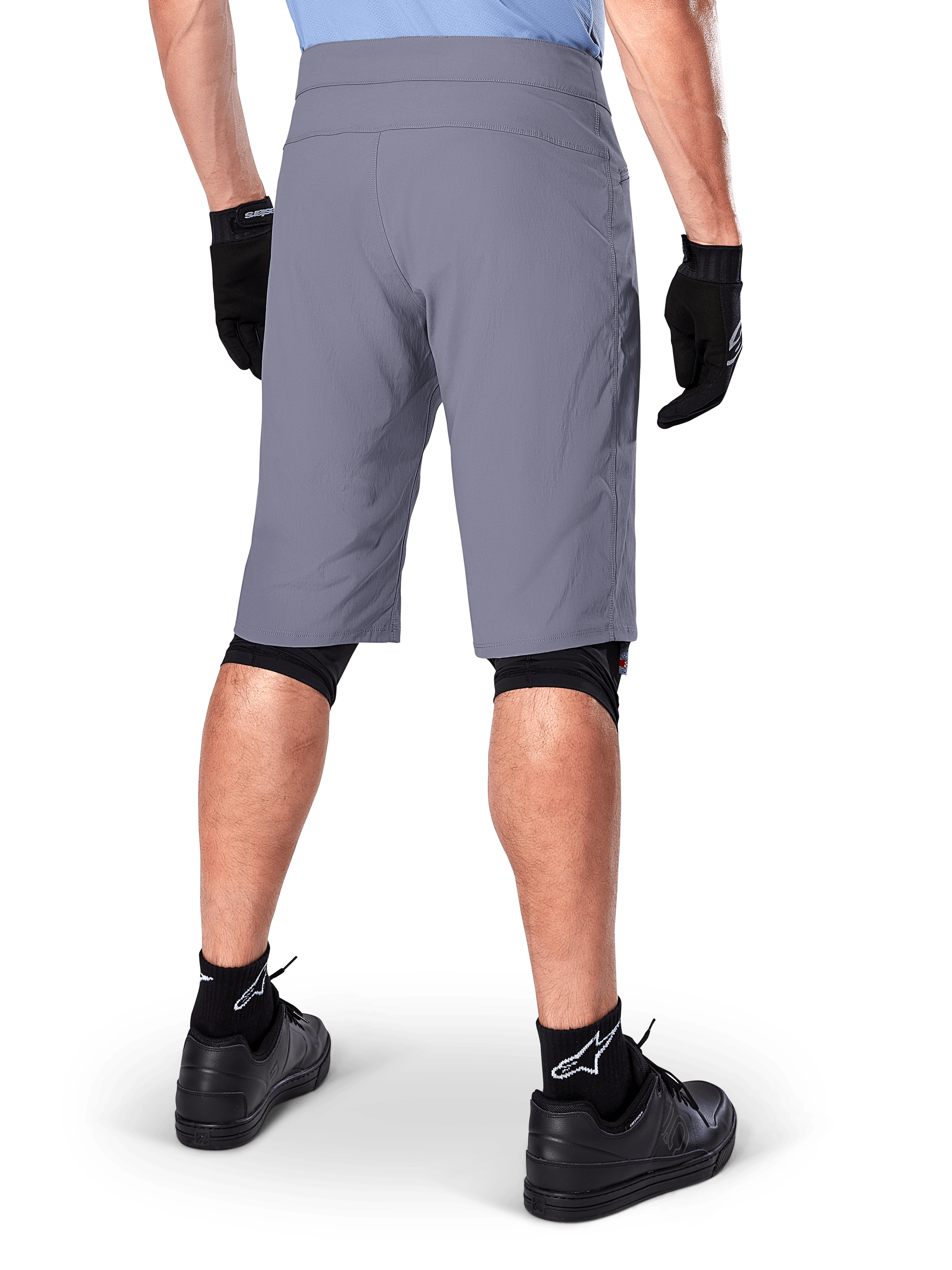 Alpinestars A-Dura Shorts, dunkelgraue Mountainbike-Shorts, Rückansicht an einem Fahrer, getragen mit schwarzen Handschuhen, schwarzen Knie-Linern und schwarzen Socken mit Alpinestars-Logo, strapazierfähige Konstruktion für den Offroad-Radsport