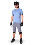 Alpinestars A-Dura Shorts, MTB-Shorts, Dunkelgrau, getragen von einem Fahrer mit einem hellblauen Trikot, schwarzem MTB-Helm, schwarzen Handschuhen und Knieschonern, komplettes Mountainbike-Outfit für Trail- und Offroad-Fahrten