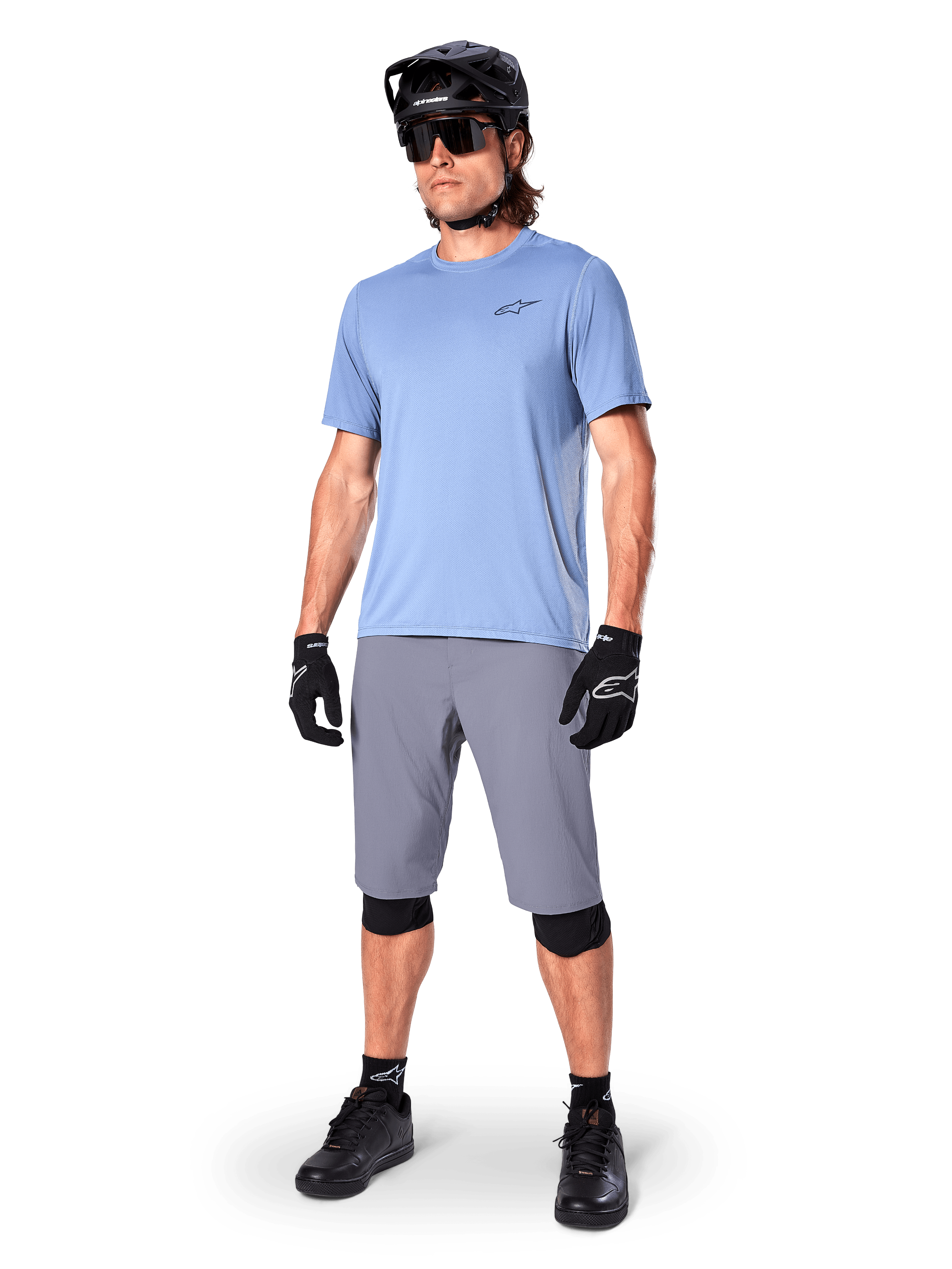 Alpinestars A-Dura Shorts, MTB-Shorts, Dunkelgrau, getragen von einem Fahrer mit einem hellblauen Trikot, schwarzem MTB-Helm, schwarzen Handschuhen und Knieschonern, komplettes Mountainbike-Outfit für Trail- und Offroad-Fahrten