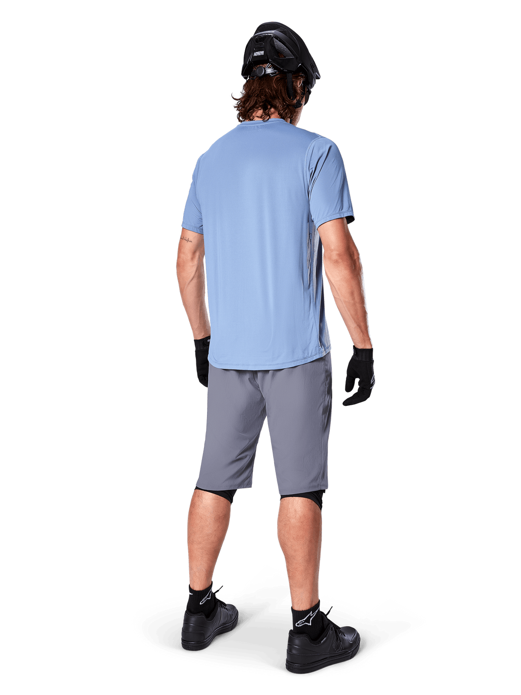 Alpinestars A-Dura Shorts, dunkelgraue MTB-Shorts, Rückansicht, getragen mit einem hellblauen Kurzarmtrikot, schwarzem Mountainbike-Helm, schwarzen Handschuhen, Socken und Schuhen, funktionelle und strapazierfähige Ausrüstung für den Offroad-Radsport