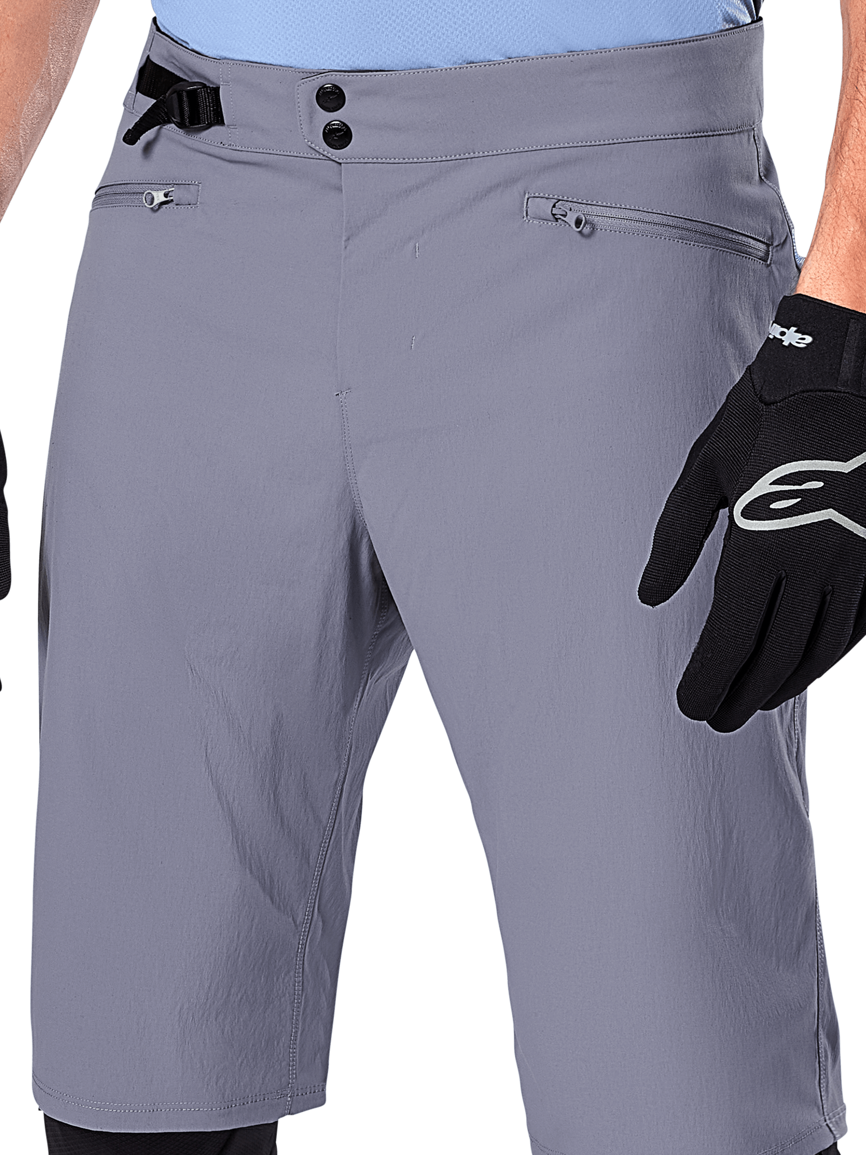 Alpinestars A-Dura Shorts, MTB-Shorts, Dunkelgrau, Nahaufnahme der Taille mit doppeltem Druckknopfverschluss, seitlichem Taillenversteller und Reißverschlusstaschen, kombiniert mit schwarzen Fahrradhandschuhen, strapazierfähige Mountainbike-Bekleidung.