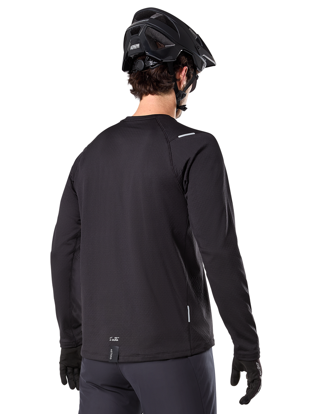 Alpinestars A-Dura Thermal Jersey, langärmeliges Mountainbike-Trikot, Schwarz, Rückansicht mit verlängertem Rückenteil, kleine reflektierende Details und Branding am Saum, getragen mit einem schwarzen Helm und Handschuhen für das Radfahren bei kaltem Wetter