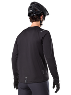 Alpinestars A-Dura Thermal Jersey, langärmeliges Mountainbike-Trikot, Schwarz, Rückansicht mit verlängertem Rückenteil, kleine reflektierende Details und Branding am Saum, getragen mit einem schwarzen Helm und Handschuhen für das Radfahren bei kaltem Wetter