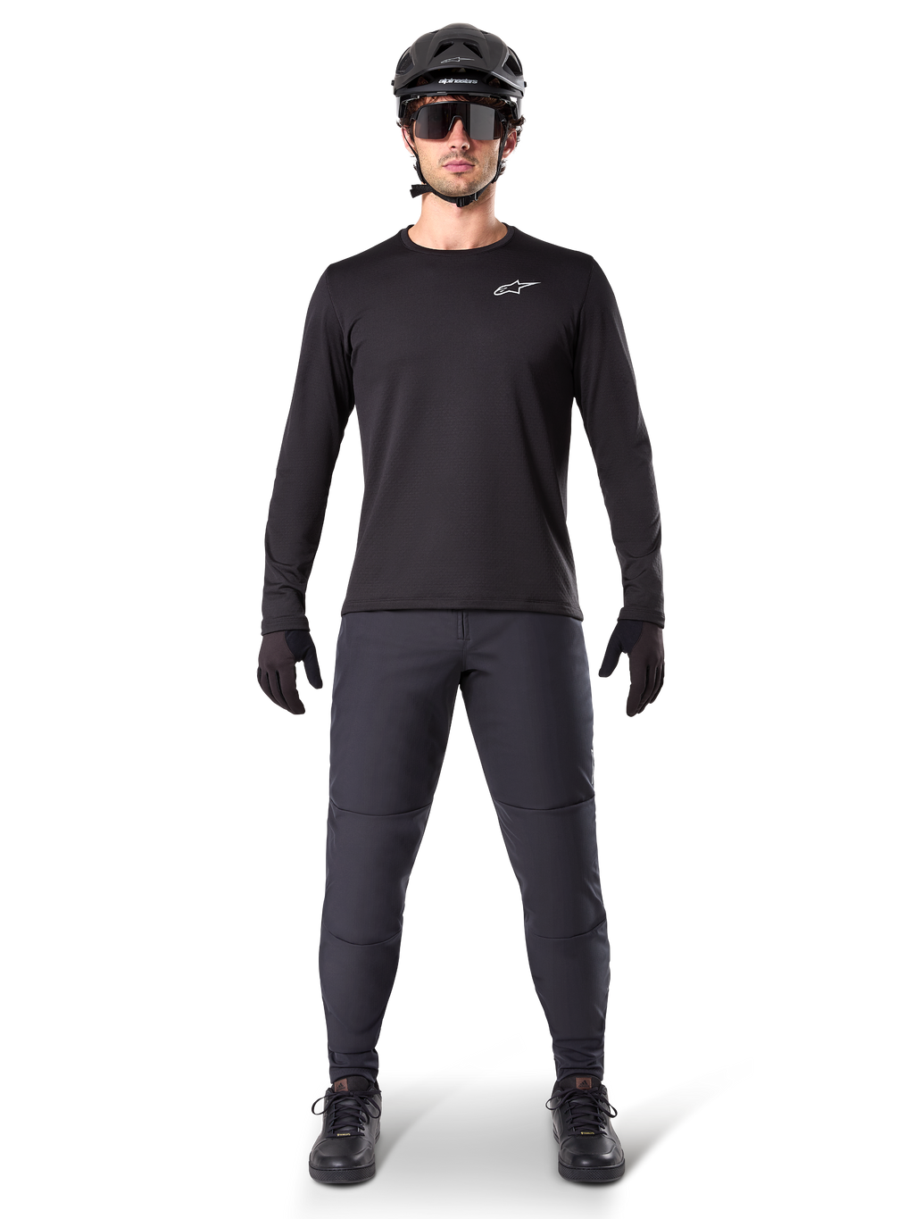 Alpinestars A-Dura Thermal Trikot, schwarzes langärmeliges Mountainbike-Trikot, kombiniert mit dunkelgrauer Hose, schwarzen Handschuhen, schwarzem Helm und Sonnenbrille, mit weißem Alpinestars-Logo auf der Brust, abgestimmtes Outfit für Mountainbiking bei kaltem Wetter