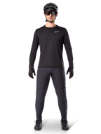 Alpinestars A-Dura Thermal Trikot, schwarzes langärmeliges Mountainbike-Trikot, kombiniert mit dunkelgrauer Hose, schwarzen Handschuhen, schwarzem Helm und Sonnenbrille, mit weißem Alpinestars-Logo auf der Brust, abgestimmtes Outfit für Mountainbiking bei kaltem Wetter
