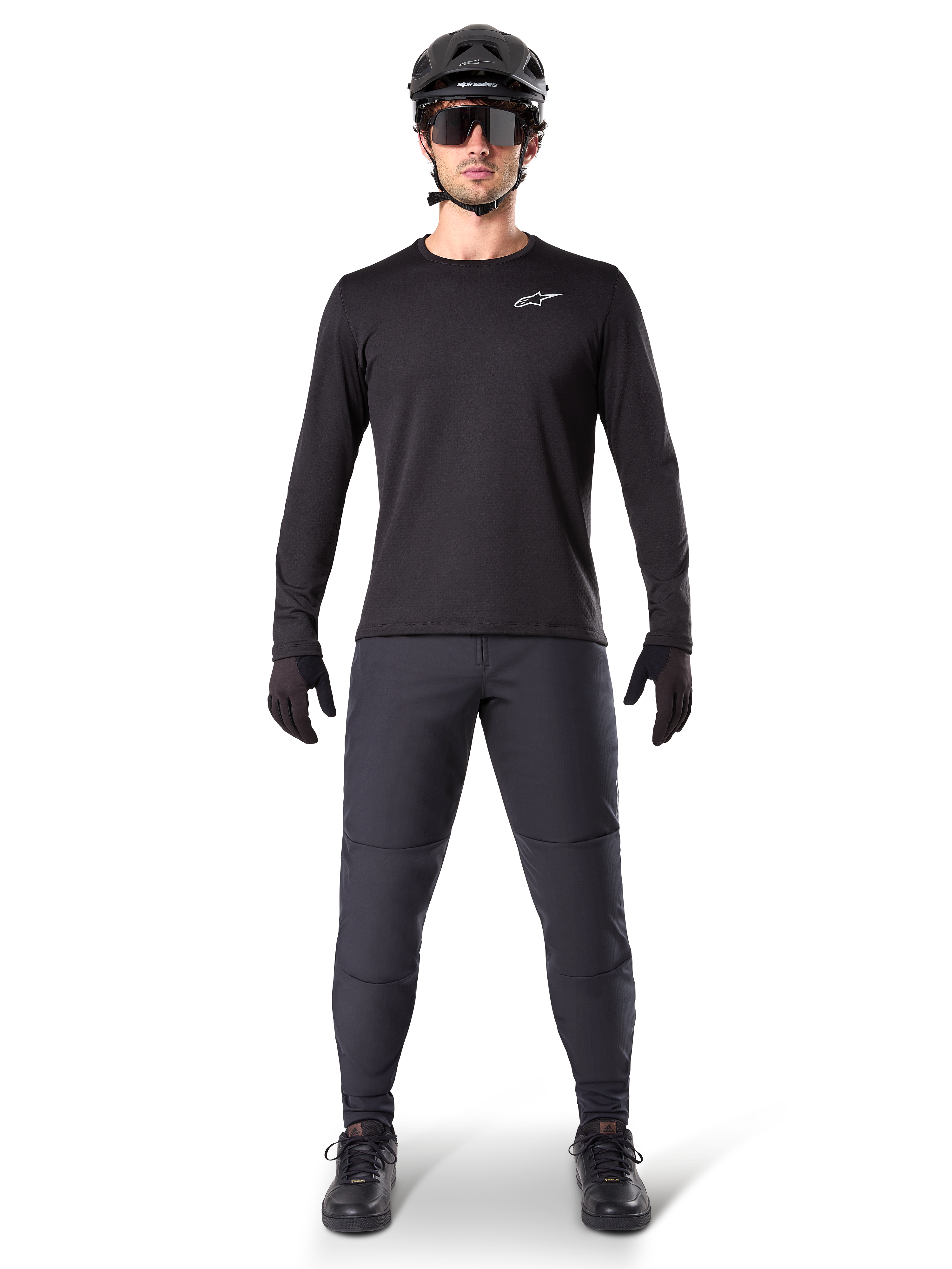 Alpinestars A-Dura Thermal Trikot, schwarzes langärmeliges Mountainbike-Trikot, kombiniert mit dunkelgrauer Hose, schwarzen Handschuhen, schwarzem Helm und Sonnenbrille, mit weißem Alpinestars-Logo auf der Brust, abgestimmtes Outfit für Mountainbiking bei kaltem Wetter
