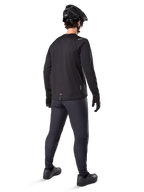 Alpinestars A-Dura Thermal Trikot, langärmeliges Herren-Radtrikot, Schwarz, Rückansicht an einem Model mit schwarzem MTB-Helm, dunkelgrauer Hose und schwarzen Handschuhen, professionelle Mountainbike-Bekleidung für kaltes Wetter